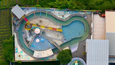 Bereketli yeşilliklerle çevrili eşsiz şekilli bir açık havuz kompleksinin havadan görünüşü, kentsel boş zamanların özünü yakalıyor. Yüksek kalite fotoğraf