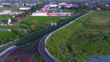 Dolambaçlı otobanı yeşil tarlaları ve dağınık binaları kesen kırsal bir şehir manzarası.