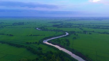 Bereketli yeşil tarlaları kesen kıvrımlı bir nehri gösteren hava manzarası, su ve tarım arazileri arasında manzaralı bir kontrastlık yaratır.