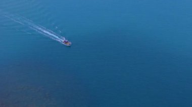 Sonsuz mavi denizi boydan boya geçen yalnız bir tekne ardında parlak bir iz bırakır.