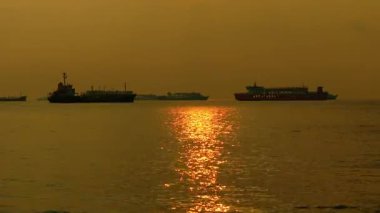 Günbatımında geniş çaplı statik çekim, içinde feribot ve kargo gemileri de bulunan birkaç gemiyi yakalar. Güneşin altın yansıması bir gökyüzünün altında su yüzeyinde parıldar. Yüksek kalite 4k görüntü