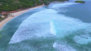 İHA çekimleri, verimli yeşillik ve uzak bir adayla çevrili el değmemiş kumlu bir sahile doğru ilerleyen güçlü turkuaz dalgalar sergiliyor. Yüksek kalite 4k görüntü