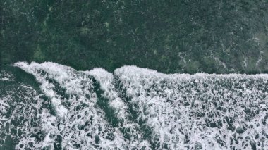 Beyaz okyanus dalgalarının yukarıdan aşağıya soyut hava görüntüsü koyu yeşil deniz yüzeyinde karmaşık köpük desenleri yaratıyor. Yüksek kalite fotoğraf