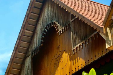 Geleneksel ahşap ev cephesine yakın plan. Karmaşık detaylar, fayanslı bir çatı ve parlak mavi gökyüzünün altında süslü saçaklar. Yüksek kalite fotoğraf