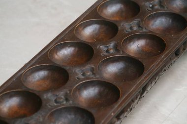 A close-up view of a traditional wooden congkak or mancala board game, featuring carved patterns and smooth, circular depressions for playing pieces. High quality photo