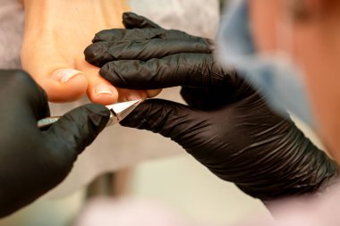 Profesyonel pedikür. Plastik eldiven giyen pedikür uzmanı güzellik salonunda kadın ayak tırnaklarını kesiyor.