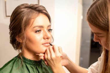 Dudak makyajı. Makyöz, güzellik salonundaki genç bir kadının dudaklarına kalemle şekil verir.