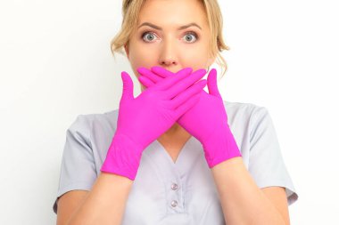 Kafkasyalı genç bir doktor ya da hemşire portresi beyaz arka planda pembe eldivenli elleriyle ağzını kapatırken şok oluyor.