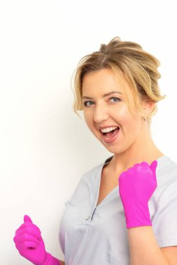 Happy caucasian woman doctor wearing pink gloves celebrates and raising fists on white background