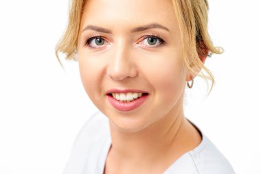 Beyaz arka planda kameraya dik dik bakan beyaz, gülümseyen beyaz kadın sağlık görevlisinin yakın plan portresi.