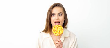 Beyaz gömlekli güzel beyaz bir kadın beyaz arka planda lolipop yalıyor.