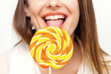 Beyaz gömlekli güzel beyaz bir kadın beyaz arka planda lolipop yalıyor.