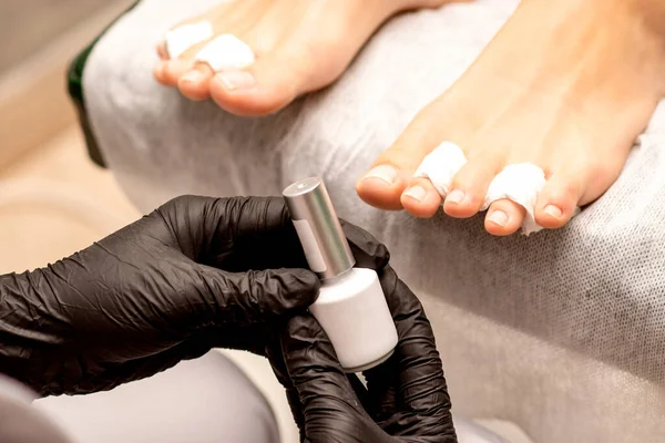 White nail polish in the hands of a manicurist while painting nails on a female feet, closeup