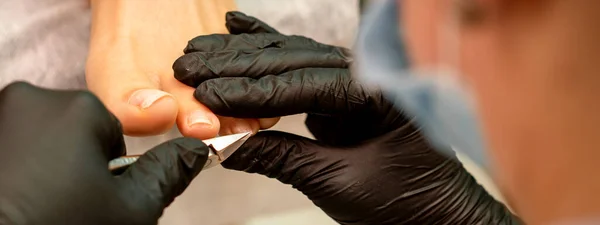 プロの映像だ ラテックス手袋を身に着けているペディキュアマスターは 美容室で女性の爪をカット クローズアップ — ストック写真