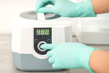 Koruyucu eldivenli güzellik uzmanı, tıbbi işlemden önce aletlerin dezenfekte edilmesi için makineyi çalıştırdı