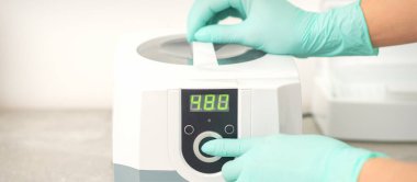 Koruyucu eldivenli güzellik uzmanı, tıbbi işlemden önce aletlerin dezenfekte edilmesi için makineyi çalıştırdı