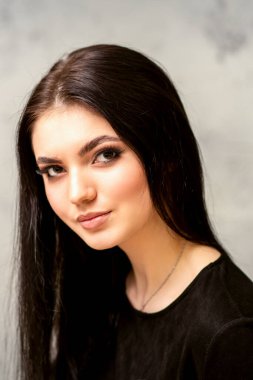 Modaya uygun genç bayan. Uzun saçlı ve makyajlı güzel kadın modelin portresi. Gri bir duvarın arkasında siyah saç stili olan beyaz bir kadın.