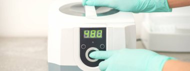 Koruyucu eldivenli güzellik uzmanı, tıbbi işlemden önce aletlerin dezenfekte edilmesi için makineyi çalıştırdı