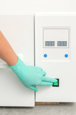 Koruyucu eldivenli güzellik uzmanı, tıbbi işlemden önce aletlerin dezenfekte edilmesi için makineyi çalıştırdı