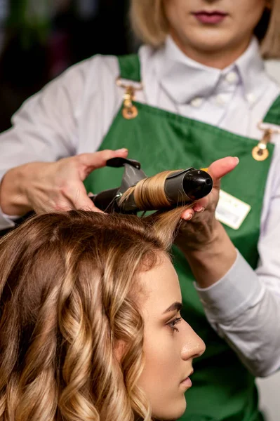 这个女理发师正在美容院里为一位棕色头发的年轻的高加索女人卷着头发 — 图库照片