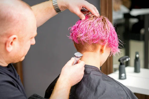 男性の美容師シェービング首の若いですCaucasian女性で短いピンクのヘアスタイルで電気シェーバーで美容室 閉じる — ストック写真