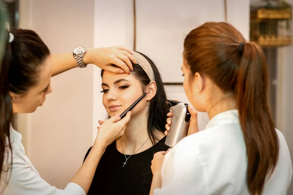 美容室で若い白人女性の顔にエアブラシを使ってメイクアーティスト — ストック写真