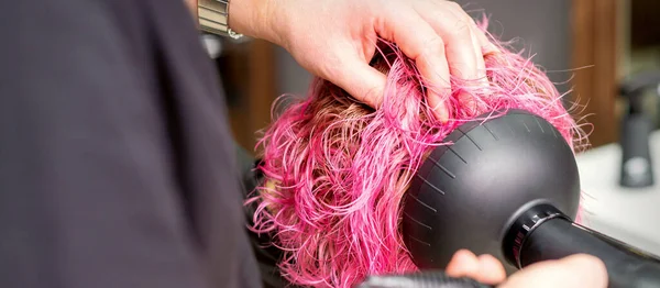 在美发厅里用男性发型师的手刷 用黑色吹风机擦干一个年轻的高加索女人的粉色短发 然后把头发关上 — 图库照片