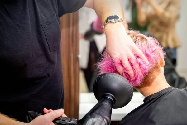 若い白人女性の短いピンクのボブの髪型を乾燥させます黒髪のドライヤーとヘアサロンで男性の美容師の手でブラシ 閉じる — ストック写真