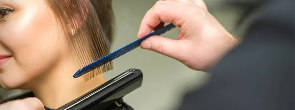 发型师正在理发店里理直一头乌黑的年轻女子的短发 她的头发是用扁平的熨斗烫的 — 图库照片