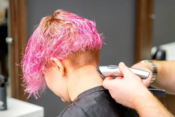 男性の美容師シェービング首の若いですCaucasian女性で短いピンクのヘアスタイルで電気シェーバーで美容室 閉じる — ストック写真