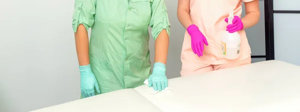 Two medical workers disinfect the patient\'s couch with sanitizer spray and a clean napkin. Health and hygiene concept