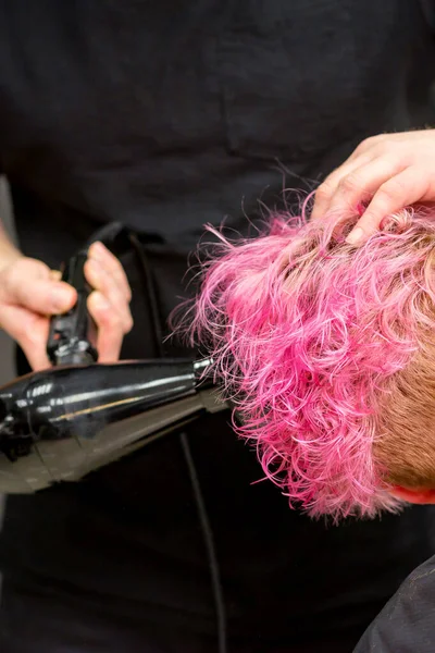 在美发厅里用男性发型师的手刷 用黑色吹风机擦干一个年轻的高加索女人的粉色短发 然后把头发关上 — 图库照片