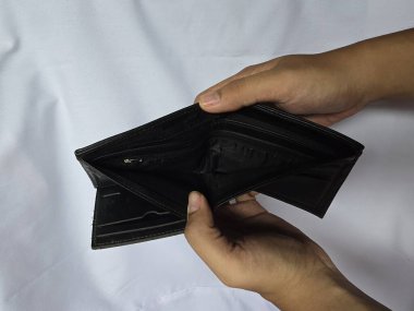 Boş bir siyah cüzdanı tutan ellerin yakın çekimi, finansal zorlukları, parasızlığı veya ekonomik zorlukları sembolize ediyor.. 