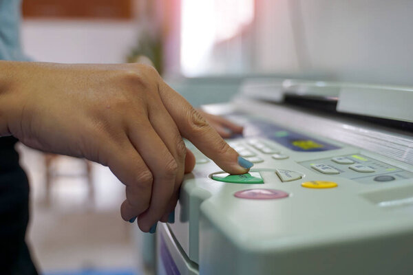 The office secretary presses the button to start the document copying machine to have another copy of the document stored in a file as evidence.                                