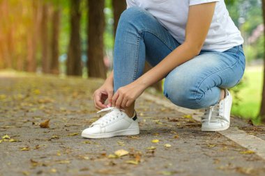 Asyalı kadın parkta yürürken bağcıklarını bağlamak için eğiliyor. Yumuşak ve seçici bir odak noktası..                                