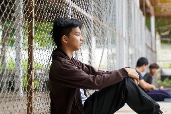 stock image young male sits with his knees bent and his hands on his knees. He looked down at the ground and thought. Sitting separated from friends. Concept of teenager, having problems, thinking, alone.                               