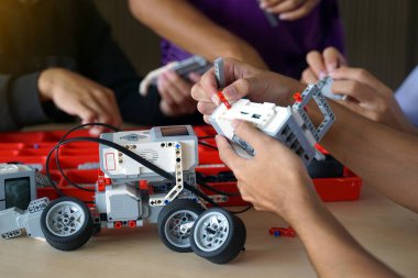 Asyalı erkek öğrenciler Robotik Kulübü 'nden arkadaşlarıyla birlikte oturuyorlar. Robot arabanın parçalarını birleştirin. Yumuşak ve seçici odak.                               
