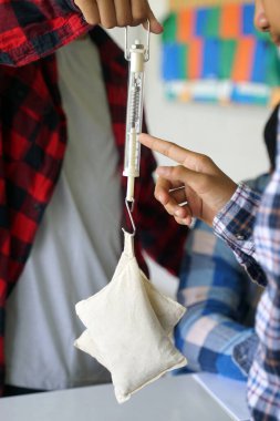 Öğrenciler, bir bahar dengesi kullanarak nesnelerin ağırlıkları üzerinde bir fizik deneyi yapıyorlar. Bilim sınıfı kavramı, öğrenme bilimi, bilim becerileri, öğrenme, bilim deneyi ve fizik.                             