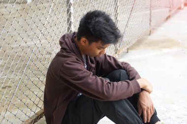 Genç erkek dizleri bükük ve elleri dizlerinin üzerinde oturuyor. O yere baktı ve düşündü. Arkadaşlardan ayrı oturmak. Gençlik kavramı, sorunlar, düşünme, yalnızlık..                           