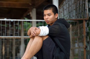 Genç erkek dizleri bükük ve elleri dizlerinin üzerinde oturuyor. O yere baktı ve düşündü. Arkadaşlardan ayrı oturmak. Gençlik kavramı, sorunlar, düşünme, yalnızlık..                               