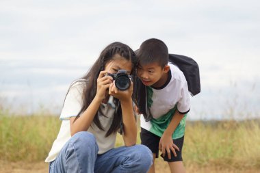 Asyalı erkek ve kız boş zamanlarında sahada doğa fotoğrafları çekmek için dijital kamera kullanıyorlar. Keşif kavramı, sınıf dışında, açık havada, ekoloji, doğa, öğrenme, seyahat.                               