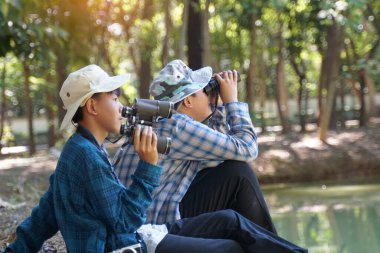 İki Asyalı çocuk yerel kuşları incelemek için bir halk ormanında dürbün kullanıyor. Yumuşak ve seçici odak.                               