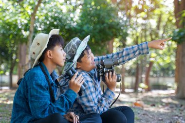 İki Asyalı çocuk yerel kuşları incelemek için bir halk ormanında dürbün kullanıyor. Yumuşak ve seçici odak.                               