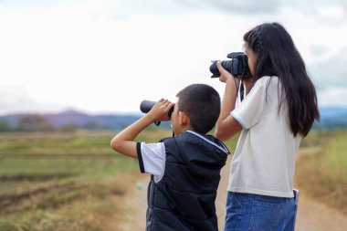 Dürbün kullanan bir oğlan ve tarlada doğayı keşfetmek için dijital kamera kullanan bir kız. Keşif kavramı, sınıf dışında, açık havada, ekoloji, doğa, öğrenme, seyahat.                               