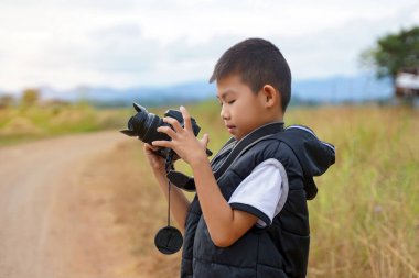 Asyalı çocuk tarlada doğa fotoğrafları çekmek için dijital kamera kullanıyor. Keşif kavramı, sınıf dışında, açık havada, ekoloji, doğa, öğrenme, seyahat.                                
