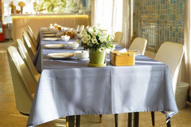 Yemek masası gri bir masa örtüsüyle kaplı, zarif görünüyor. Masanın üzerinde, bir sofra takımı güzelce düzenlenir ve kullanıma hazır hale getirilir, ve bir vazo çiçekle süslenir..                               