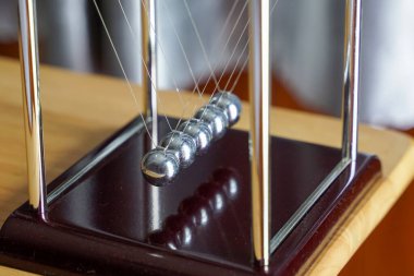 Newton 'un beşiği momentumun korunmasını ve sallanan kürelerle enerjinin korunmasını gösteren bir cihazdır. Yumuşak ve seçici odak.                               