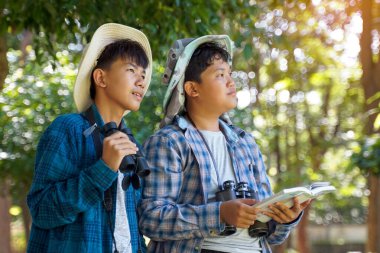 İki Asyalı çocuk yerel kuşları incelemek için bir halk ormanında dürbün kullanıyor. Yumuşak ve seçici odak.                               