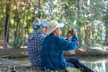 İki Asyalı çocuk yerel kuşları incelemek için dürbün ve kamera kullanıyor. Yumuşak ve seçici odak.                               