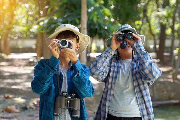 İki Asyalı çocuk yerel kuşları incelemek için dürbün ve kamera kullanıyor. Yumuşak ve seçici odak.                                